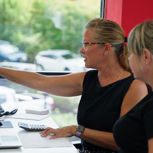 Two people in an office environment, there is a calculator and paperwork on a desk