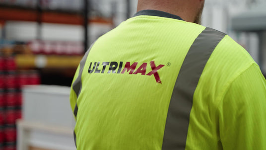 Person wearing a bright yellow safety vest with 'Ultrimax' branding in an indoor setting.