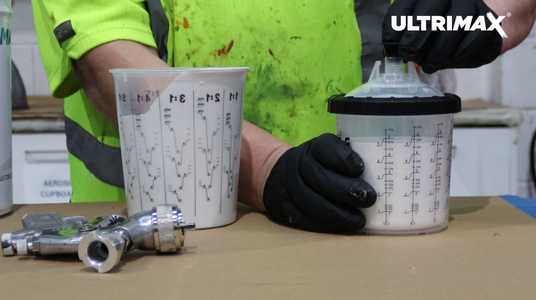 Person using ULTRIMAX branded equipment with measuring cups and tools on a table.