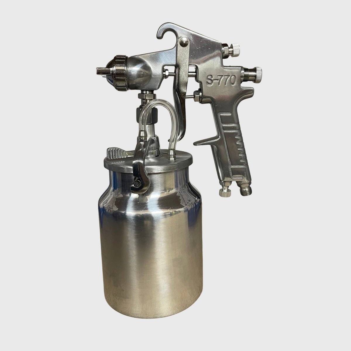 Stainless steel suction feed spray gun showing the nozzle, trigger, and attached paint reservoir